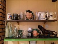 Shelf with Toby jugs, steins, glass mugs, and bronze tiger figurine.