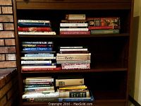 Wide view of three shelves filled with a variety of cookbooks, showing many colorful and vintage titles.