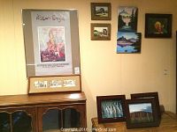 View of wall with multiple framed artworks including Nissan Engel signed poster, Vera Sorensen watercolors, Ogunquit signed watercolors, and framed photos of terra cotta warriors, Ayers Rock and tulip.