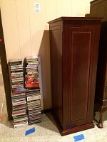 Closed wooden media cabinet standing next to stacks of CDs and cassette tapes.