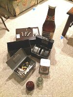 Overview of lot on carpet including storage boxes, knives on a board, large bottle replica, and small tins.