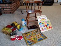 Photo showing wooden child's chair with Tonka tractor and car toys, coin changer, puzzles, and other various vintage children's items arranged on carpet.