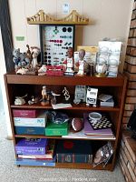 Wide shot of wooden shelf displaying bridge model, button display, animal and metal figurines, games, books, football and chess board