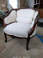 Front view of carved wooden armchair with white fabric upholstery and matching bolster pillow