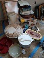 Photo showing various kitchenware including stacking white plastic bowls with lids, ceramic watermelon bowl, red divided tray, and folded table linens in background.