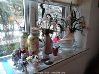 Wide shot showing Royal Bonn vases, porcelain figurines, pottery planters, and glass bowls on windowsill.