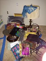 Photo showing multiple ladies accessories including colorful silk scarves, several beaded handbags of different colors and styles, a table lamp with a white fringed shade, and a purple travel iron.