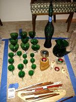 Overview of assorted green stemware glasses, decanter with stopper, wooden chopsticks, and napkin rings arranged on carpet under chair