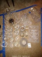 Top-down view of large assortment of glassware and crystal items arranged on carpet including shrimp cups, salt dishes, stemware and decanters.