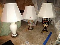 Three ceramic base lamps positioned on carpet: white, floral design, and black classical style.