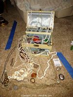 Full view of assorted costume jewelry laid out with a multi-tiered jewelry box and loose pieces including necklaces, brooches, pins, and watches.