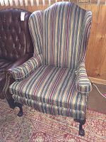 Front view of a wingback armchair with striped upholstery, curved armrests, and carved wooden legs.