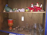 Shelf with assorted decorative glassware including clear glasses and a gold-orange colored pitcher