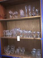 Three wooden shelves filled with various clear glassware including champagne flutes, dessert cups, and wine glasses.