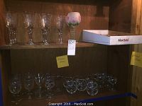 Top shelf with assorted clear stemmed wine glasses and hand painted floral wine glass on right