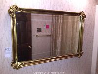Front angled view of the rectangular mirror hanging on a floral wallpapered wall, showing the entire frame and reflective surface.