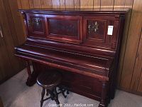 Front view of Sterling upright piano with decorative veneer inlays and attached candle holders, with rotating stool in front.