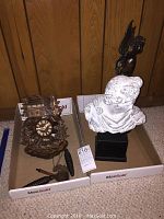 Photo showing the cuckoo clock with pine cones weights, white bust replica with cupid statue sitting on top, all placed in cardboard trays.