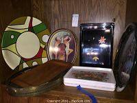 Multiple serving trays displayed on a wooden shelf including round, oval, floral, and black trays.