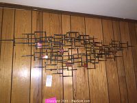 Front elevation of abstract metal sculpture mounted on wood-paneled wall.