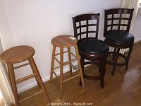 Four seating items: two wooden stools with natural wood finish and two dark wood swivel chairs with black leather seats, arranged against wall on wood floor.