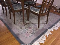Floral area rug under dining table showing flower patterns and white fringed edges on wood floor.