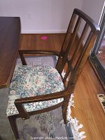 Side view of wooden dining chair with floral upholstered seat and armrests next to a dining table.