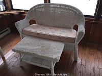 White wicker sofa with floral cushion and wicker coffee table shown together, placed on wood floor near windows.