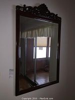 Front view of the rectangular mirror hanging on the wall, showing the reflection of a room window and decorations.