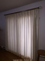 Full view of pleated curtains hanging on rod covering a window.