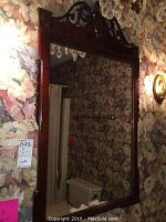 Front view of the wall mirror showing the ornate dark wood frame and floral wallpaper reflection.