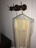 Cream-colored damask patterned tablecloth and napkin on wooden coat rack hooked on wire hanger covered in plastic
