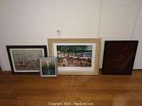 Group of four framed artworks leaning against wall on hardwood floor