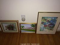 Three framed art pieces side by side against white wall showing different subjects: floral, landscape, birds.