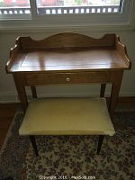 Front view of wooden vanity/writing desk with upholstered stool in front, showing details of wood grain and drawer knob.