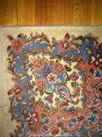 Close-up corner of rug showing blue background, floral motif with pink and brown highlights.