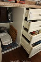 Overview showing open door to cupboard with wooden canister set, Corelle serving platter placed on bottom shelf, wooden cutting board, and metal pans beneath in lower cupboard.