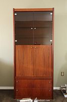 Full front view of the tall wooden storage cabinet showing two glass doors on the top, two wooden doors in the center, and two drawers at the bottom