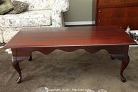 Front view of dark wood coffee table showing rectangular smooth top and cabriole legs.