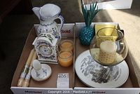 Overview of the entire decorative lot showing clock, pitcher, various candles, pineapple glass ornament and plates inside a box