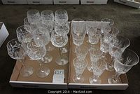Full lot of 24 cut crystal wine glasses in various types, arranged in two trays on carpet.