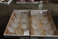 Overview of the decanter, six thistle pattern whiskey glasses, and eight frosted textured glasses arranged in two trays.