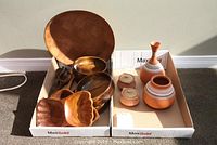 Four wooden salad bowls, a pair of wooden salad tongs, a large round wooden serving tray, and five decorative pottery pieces including vases and lidded jars in a cardboard box.