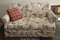 Front view of floral patterned sofa bed with plaid cushion on brown carpet.