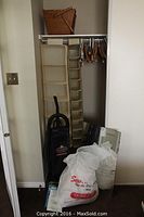 Wide view of closet contents showing Hoover vacuum, fabric hanging organizers, plastic hangers, wicker basket on shelf, and white sheer fabric in plastic bag on floor.
