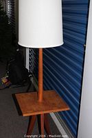 Full view of the teak floor lamp with table top and white fabric lampshade in front of a blue storage unit door.
