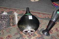 Various contemporary vases including rounded matte black vase, teardrop black vase, and tall grey metal vase displayed on rugs.