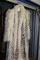 Front view of the full-length fox fur coat hanging on a wooden hanger showing the chevron fur pattern with cream and brown color tones.
