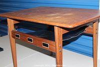 Full side view of teak table showing rectangular top and leather sling underneath