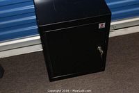 Black metal lock box closed with visible lock and keys inserted, placed on floor.